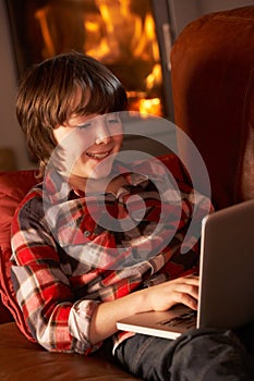 Young Boy Relaxing With Laptop By Cosy Log Fire