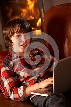 Young Boy Relaxing With Laptop By Cosy Log Fire