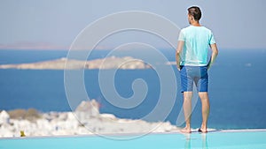Young boy relaxing near pool with amazing view on Mykonos, Greece. Beautiful famous background
