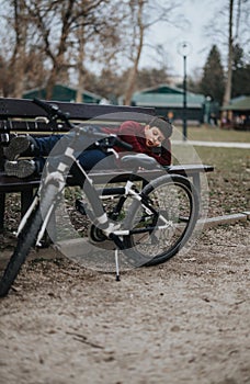 Young boy resting on a bench with his bicycle at the park