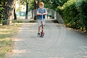 Young boy rides a scooter on the road in summer
