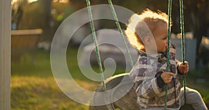 A young boy rides a swing in slow motion in the sun. Light from the sun enters the camera.
