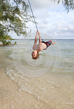 Young boy  on rope swing over ocean water