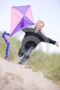 Young boy running on beach with kite smiling