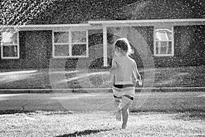 A Young Boy Running Through a Sprinkler in the Yard