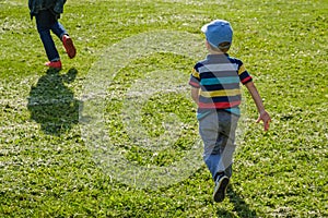 Young boy runs in a green field. Cute child running across park outdoors grass.