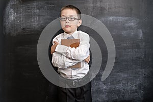 Young boy`s holding a book near blackboard. Back to school concept. Smart and clever preschool boy