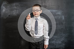 Young boy`s holding a chalk near blackboard. Back to school concept. Smart and clever preschool boy