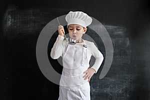 Young boy`s standing near blackboard checking soup. Young chef boy. Creative design concept for 2019 calendar.