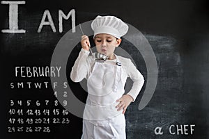 Young boy`s standing near blackboard checking soup. Young chef boy. Creative design concept for 2019 calendar. February