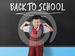 Young boy in school uniform infornt of black board with `back to school` written in white chalk