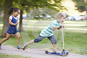 Young Boy On Scooter In Park With Sister