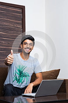 Young boy showing thumbs up and smiling while looking into the camera and laptop on table
