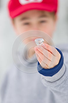Young boy shows a little piece of ice in hand at winter time, outdoors.