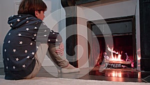 Young boy sit in front of fireplace looking at fire getting warm