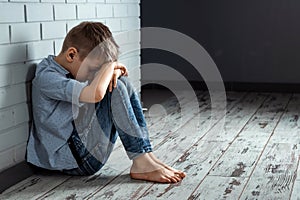 A young boy sits alone with a sad feeling at school near the wall. Offended child abandoned in the corridor and bent against a