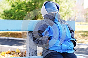 Young boy sitting on a bench with his face covered