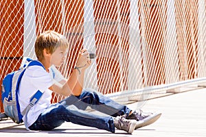 Young boy sitting with a digital camera and taking pictures in the street