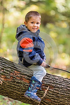 Young boy is sitting on Fallen Down Tree Trunk and play with a sword