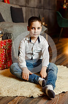 Young boy sitting on floor next to Christmas tree. Family holidays