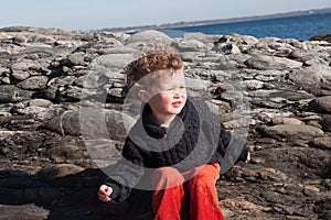 Young boy sitting near rocks at ocean