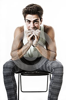 Young boy sitting resting elbows on legs, hands front mouth. On white