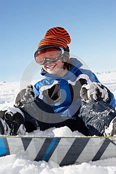 Young Boy Sitting In Snow With Snowboard