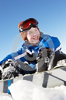 Young Boy Sitting In Snow With Snowboard