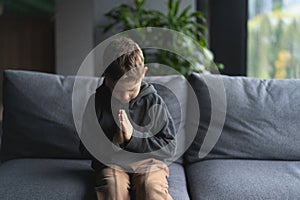 Young Boy Sitting on a Sofa With Hands Clasped in a Moment of praying
