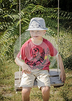 Young boy sitting on swing wearing hat