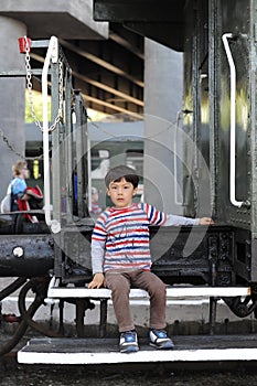 A young boy sitting between train carriages or wagons on a train station