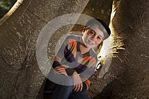 Young boy sitting beside tree trunk