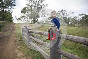 Young boy sitting on a weathered post and rail fence on a farm in Toowoomba