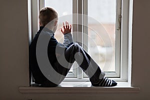 Young boy sitting on a windowsill waving