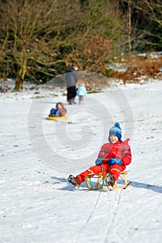 Young boy in sledge sliding snowy hill, winter fun