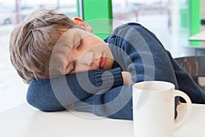 Young boy is sleeping on table with empty cup