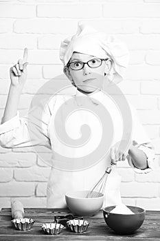 Young boy small cute cook chef in white uniform and hat on surprised face with glasses standing near table with rolling