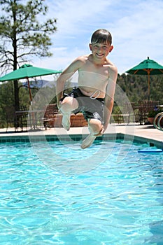 Young boy smiling and jumping into a swimming pool