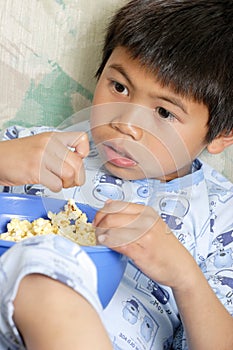 Niño comiendo palomitas mientras ve una película en casa.