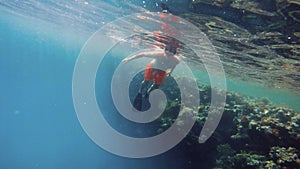 Young boy snorkel swim in shallow water with coral fish