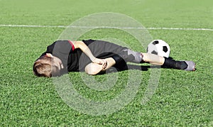 A young boy soccer player injured his leg during the match and ball on the field. Kids injury in sport concept. Copy