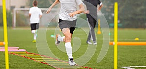 Young boy in soccer shoes cleats running through training ladder. Coach in the background