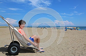 Young boy on the special wheelchair in summertime on the beach