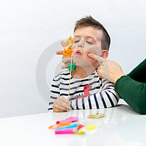 Young boy in speech therapy office. Preschooler exercising correct pronunciation with speech therapist.