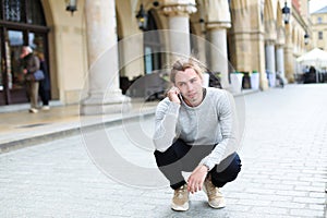 Young boy squating ad talking by smartphone outside near building.
