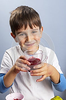 Young boy squeezing and drinking pomegranate juice, making a mess. Face and clothes dirty with red spots.