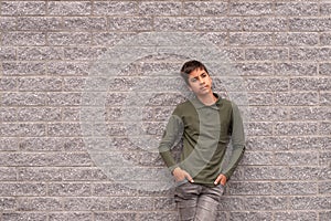 A young boy  standing against a textured brick grey wall