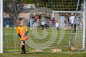 Young boy standing in front of soccer goal playing goalie during game