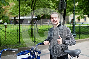 Young boy standing with hired bike near park with green trees.