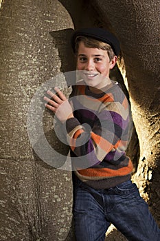 Young boy standing beside tree trunk